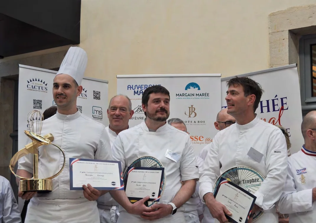 Trois lauréats sur le podium, diplôme en main, l'un d'eux tenant le trophée doré